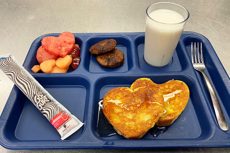 Heart-shaped french toast, fruit salad, sausage, yogurt, and glass of milk