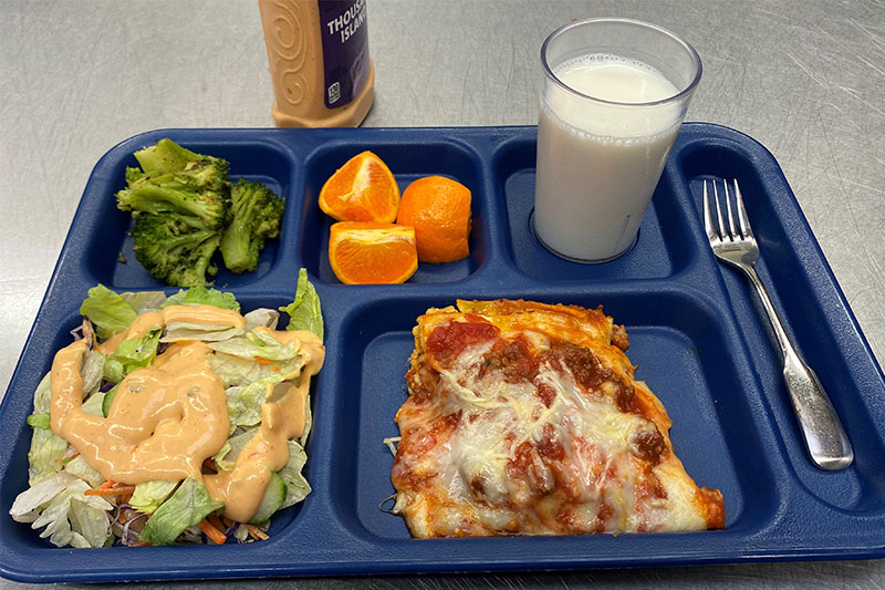 Lasagna, thousand island salad, orange slices, seasoned broccoli, with milk on tray with fork