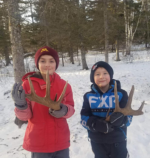 Two students holding up antlers outside in the snow