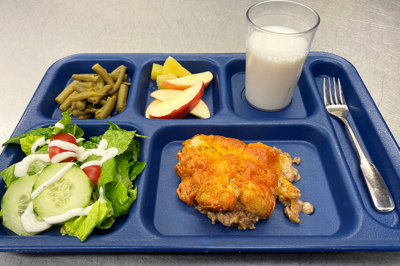 Tater tot hotdish, salad, green beans, apple slices, and a glass of milk