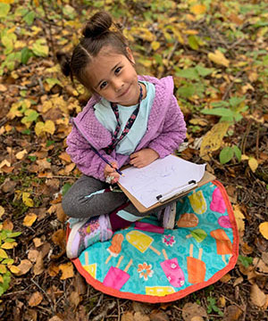 Girl drawing while sitting in the autumn leaves