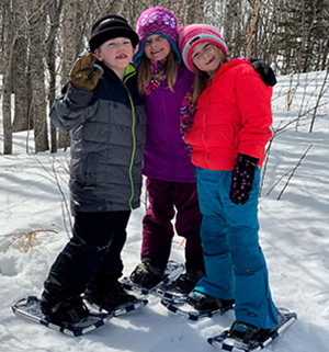 Three kids smiling and wearing snowshoes