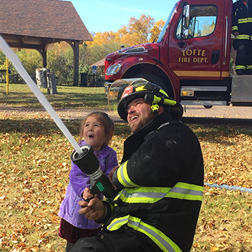 Local fireman showing amazed little girl how to use the fire hose