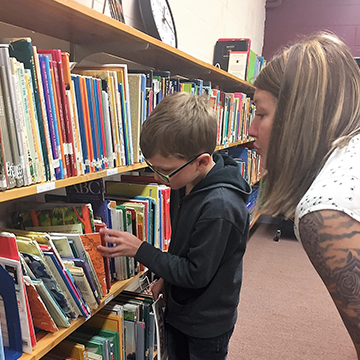 Adult helping student look for books in the library